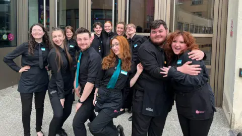 BBC Theatre staff in all black posing outside as a group outside of glass theatre doors